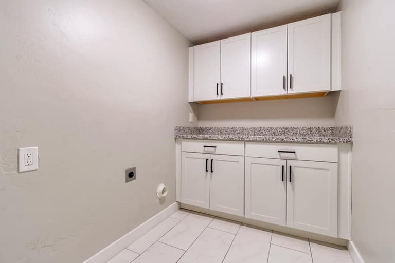Basement laundry room with white shaker cabinets, granite countertop, washer/dryer hookups, and tile floor — Utah basement laundry by CasaMás Construction