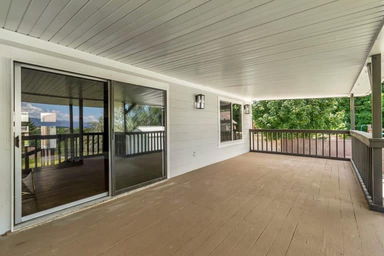 Covered back deck with white shiplap ceiling, composite decking, dark metal railings, and Utah mountain views through the railing line — by CasaMás Construction