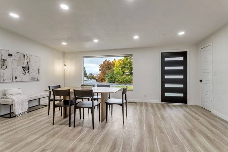Open dining area with modern black entry door, light-wood plank flooring, and large picture window — Utah dining room addition by CasaMás Construction
