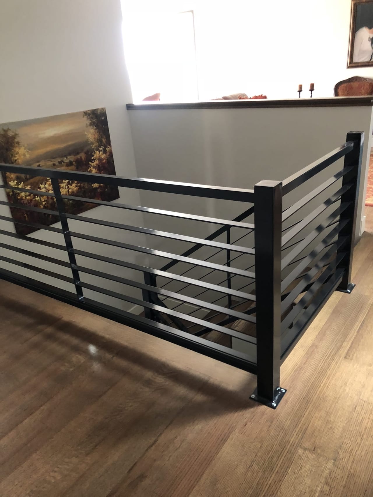Interior horizontal-slat black metal railing along loft edge, with hardwood floor and framed landscape painting — Utah interior railing by CasaMás Construction