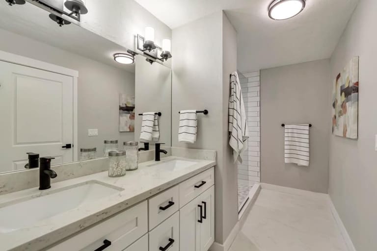 Master bathroom with double vanity, white shaker cabinets, black hardware, large mirror, and glass-enclosed shower with subway tile — Utah master bath by CasaMás Construction