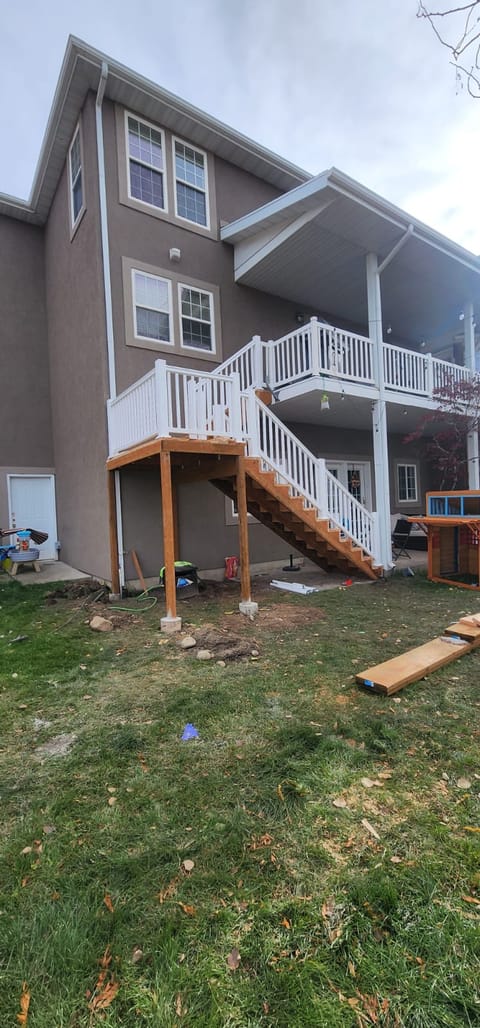 Two-story deck system with white railings and wood connecting stairs on a stucco home — Utah two-story deck by CasaMás Construction